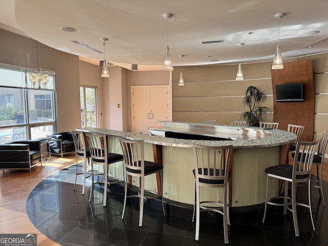 kitchen with visible vents, decorative light fixtures, light stone counters, a spacious island, and dark wood finished floors