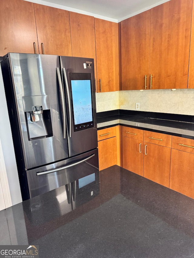 kitchen with dark stone counters, tasteful backsplash, brown cabinetry, and stainless steel refrigerator with ice dispenser