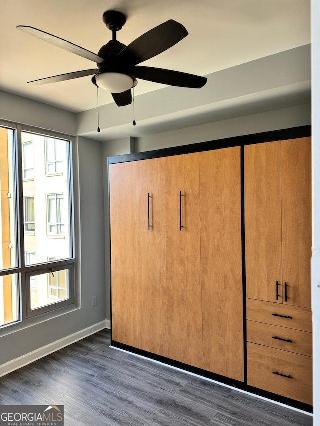 unfurnished bedroom featuring multiple windows, baseboards, and dark wood-style flooring