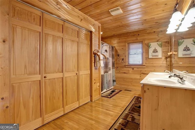 bathroom with a sink, wood finished floors, wooden walls, an inviting chandelier, and wooden ceiling