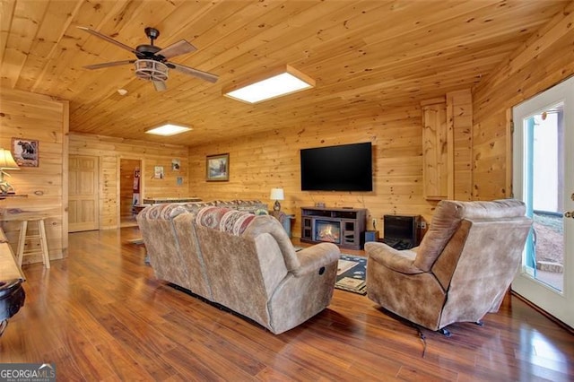 living area featuring wooden walls, wood ceiling, ceiling fan, and wood finished floors