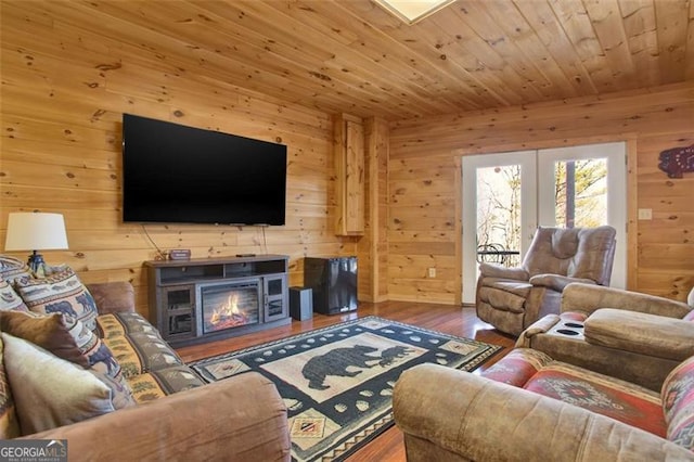 living room featuring a glass covered fireplace, wood finished floors, french doors, wooden ceiling, and wood walls