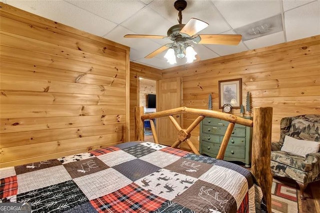 bedroom with a paneled ceiling, wooden walls, and ceiling fan