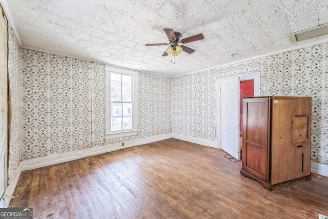 empty room featuring baseboards, wallpapered walls, ceiling fan, hardwood / wood-style flooring, and crown molding