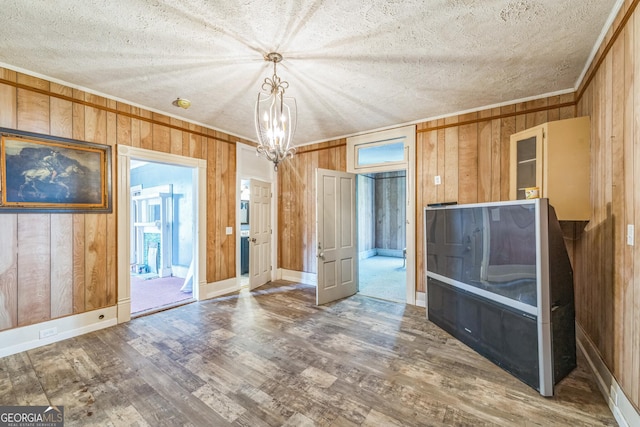 spare room with wooden walls, wood finished floors, an inviting chandelier, ornamental molding, and a textured ceiling