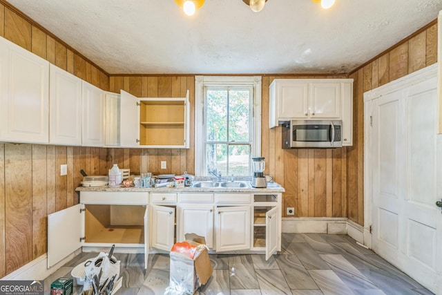 kitchen featuring wooden walls, a sink, light countertops, white cabinets, and stainless steel microwave