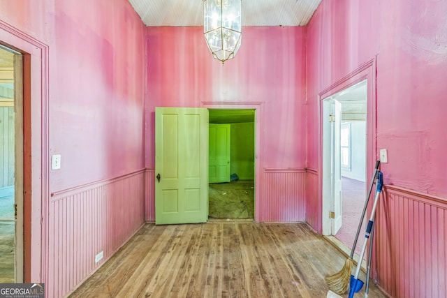 hall with wood finished floors and a wainscoted wall