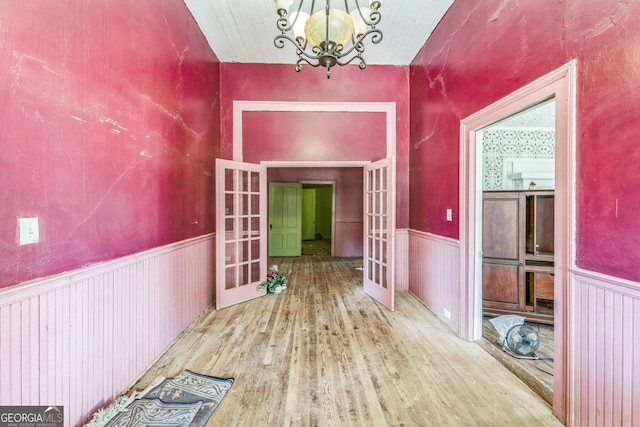 hallway with french doors, wood finished floors, a wainscoted wall, and a chandelier