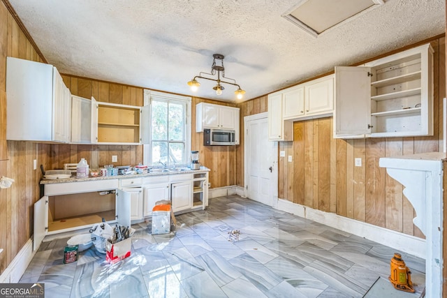 kitchen featuring wooden walls, open shelves, a textured ceiling, white cabinetry, and stainless steel microwave