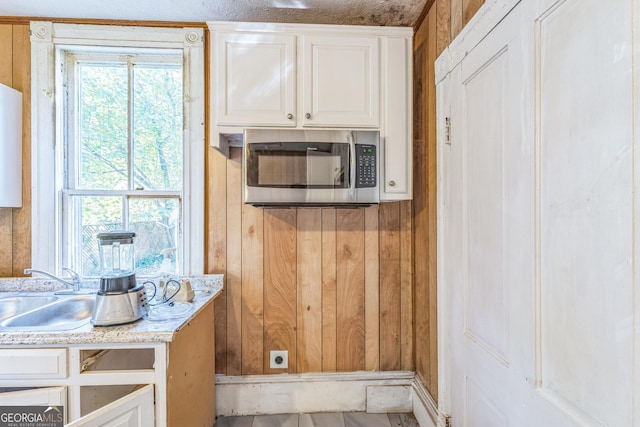 kitchen featuring white cabinetry, stainless steel microwave, and wood walls