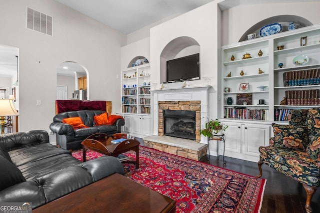 living room with visible vents, built in shelves, wood finished floors, arched walkways, and a fireplace