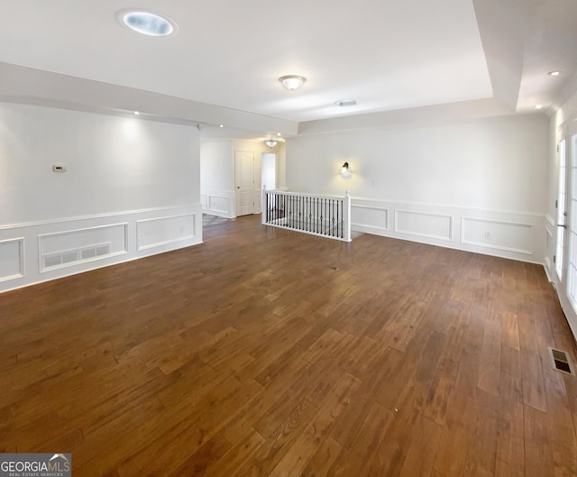 unfurnished room featuring a decorative wall, visible vents, and dark wood-style flooring