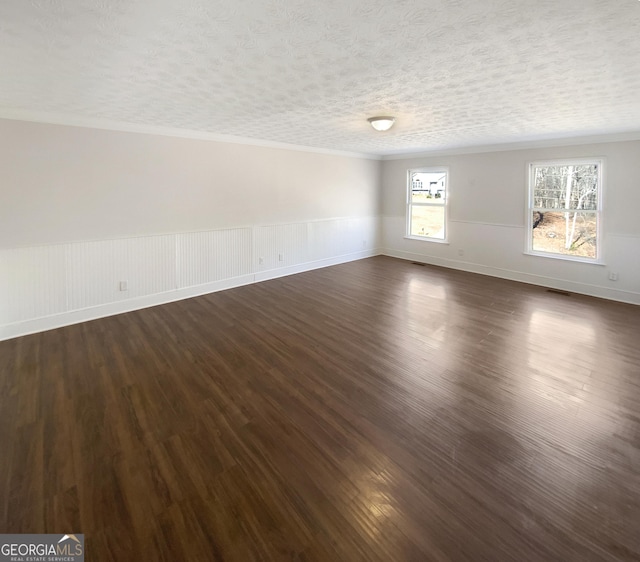 spare room with a textured ceiling, dark wood finished floors, wainscoting, and ornamental molding