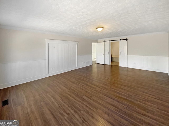 interior space with visible vents, dark wood-type flooring, a wainscoted wall, a barn door, and a textured ceiling