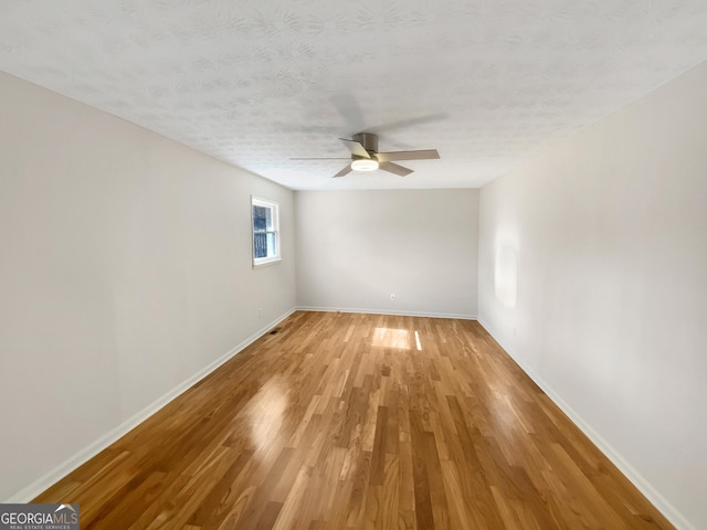 empty room featuring light wood-style flooring, a ceiling fan, baseboards, and a textured ceiling