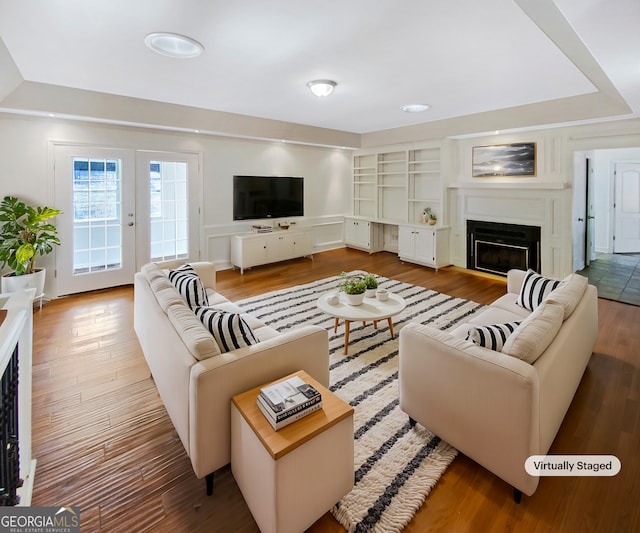 living area featuring built in shelves, wood finished floors, and a glass covered fireplace