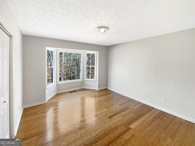 spare room featuring visible vents, baseboards, a textured ceiling, and wood finished floors