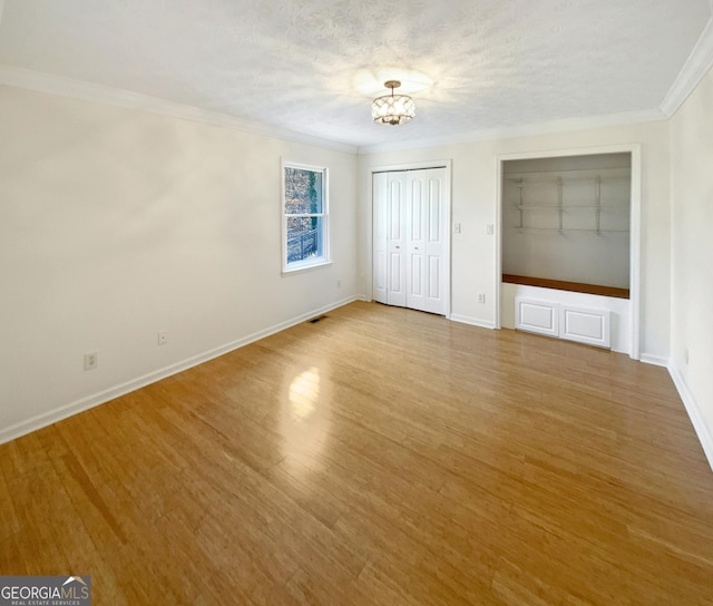 unfurnished bedroom with baseboards, a chandelier, ornamental molding, wood finished floors, and a textured ceiling