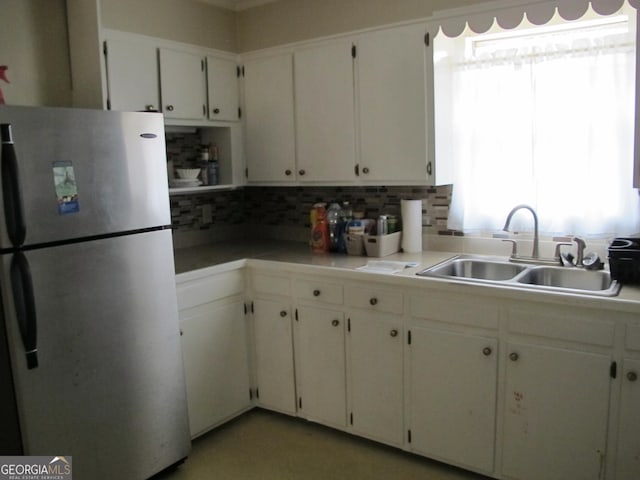 kitchen featuring tasteful backsplash, light countertops, freestanding refrigerator, and a sink