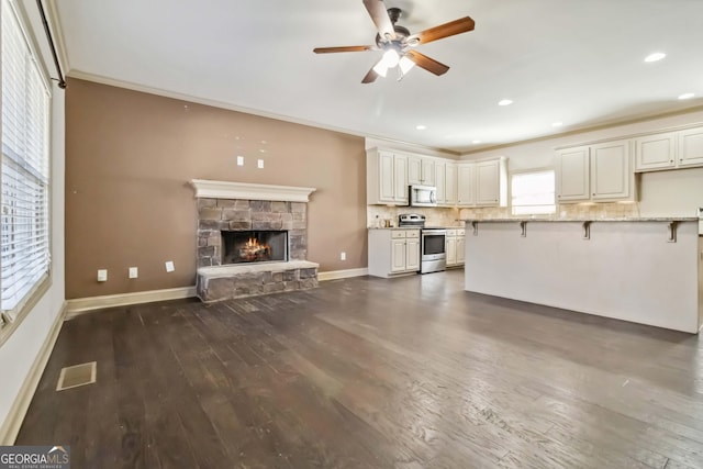 unfurnished living room with visible vents, dark wood-type flooring, crown molding, ceiling fan, and a stone fireplace