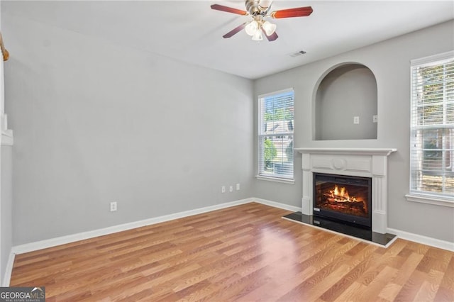 unfurnished living room with baseboards, visible vents, light wood finished floors, ceiling fan, and a glass covered fireplace