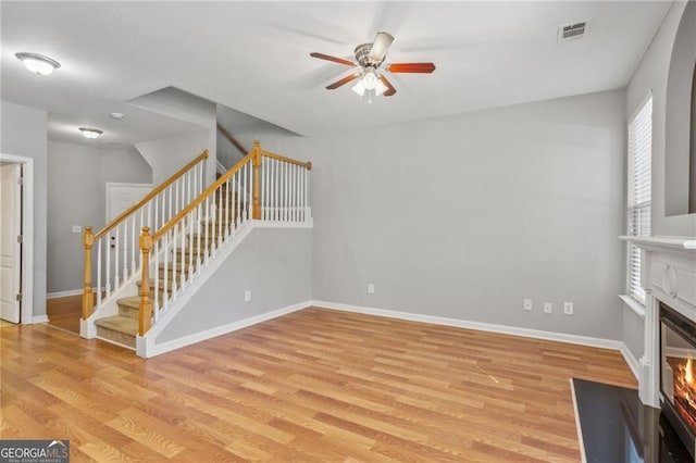 unfurnished living room with light wood-style floors, visible vents, stairs, and a ceiling fan