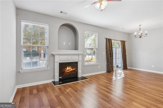 unfurnished living room with visible vents, ceiling fan with notable chandelier, wood finished floors, a glass covered fireplace, and baseboards