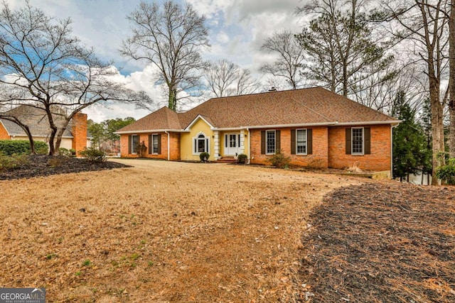 ranch-style home with brick siding, roof with shingles, and a front lawn