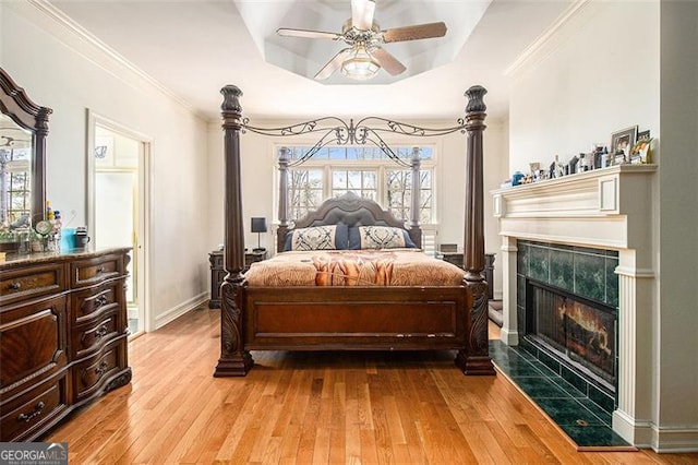 bedroom with light wood finished floors, multiple windows, a fireplace, and a raised ceiling