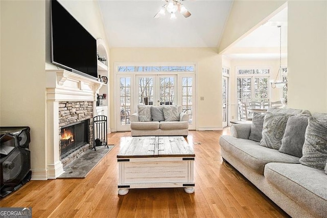 living room with built in shelves, baseboards, a stone fireplace, a ceiling fan, and wood-type flooring