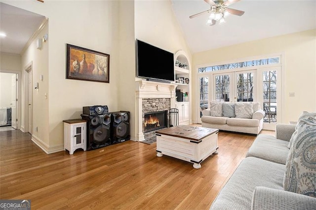 living room featuring built in shelves, a ceiling fan, high vaulted ceiling, a fireplace, and light wood-style floors