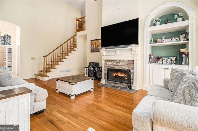 living room with built in features, wood finished floors, a high ceiling, a fireplace, and stairs