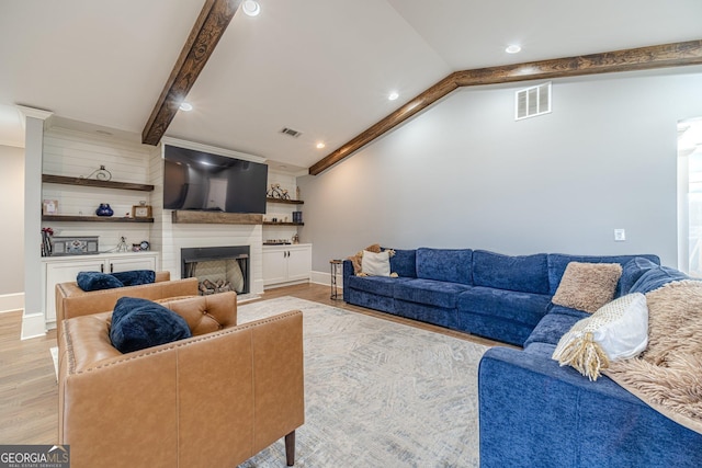 living room with light wood finished floors, visible vents, vaulted ceiling with beams, and a large fireplace