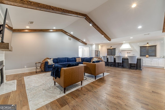 living room featuring baseboards, a fireplace, vaulted ceiling with beams, and light wood-style floors