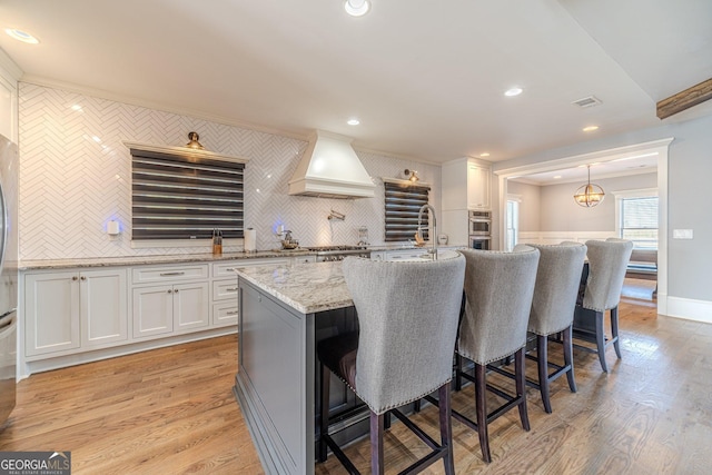 kitchen featuring a breakfast bar, custom range hood, light wood-style floors, and a sink