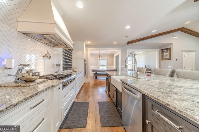 kitchen with light stone countertops, premium range hood, a sink, stainless steel appliances, and light wood-style floors