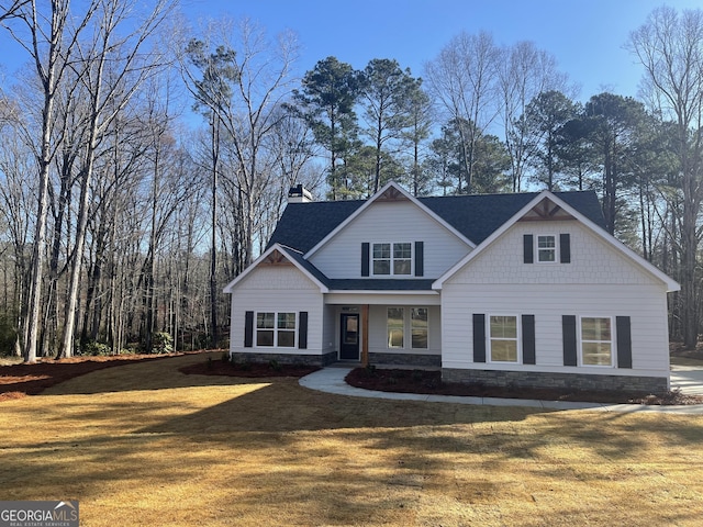 craftsman-style home with stone siding, a chimney, a front yard, and a shingled roof