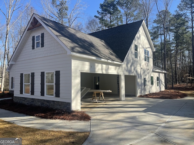 view of property exterior featuring stone siding, driveway, and a shingled roof