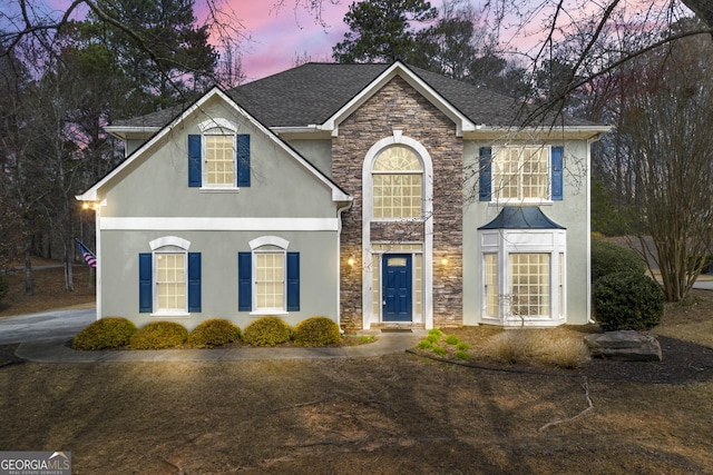 traditional-style house featuring stone siding, stucco siding, and a shingled roof