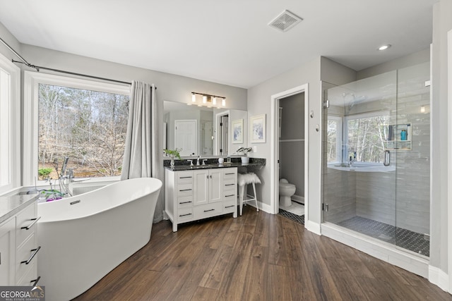 bathroom with visible vents, toilet, a stall shower, wood finished floors, and vanity