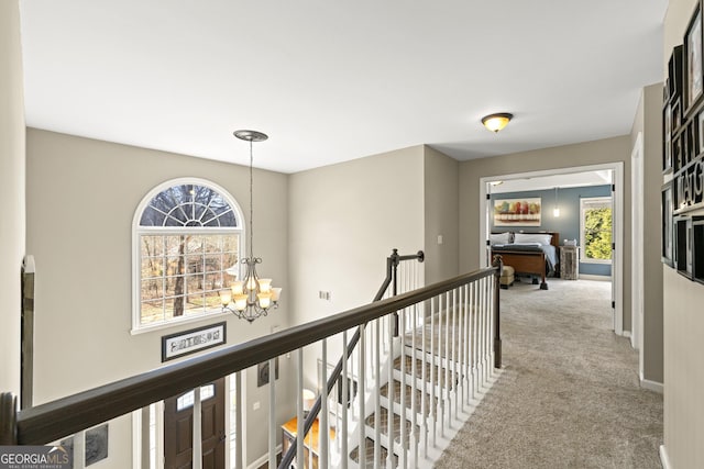 hallway featuring an upstairs landing, carpet, a healthy amount of sunlight, and a chandelier