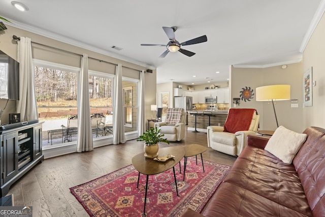 living area with a wealth of natural light, visible vents, ceiling fan, and wood finished floors