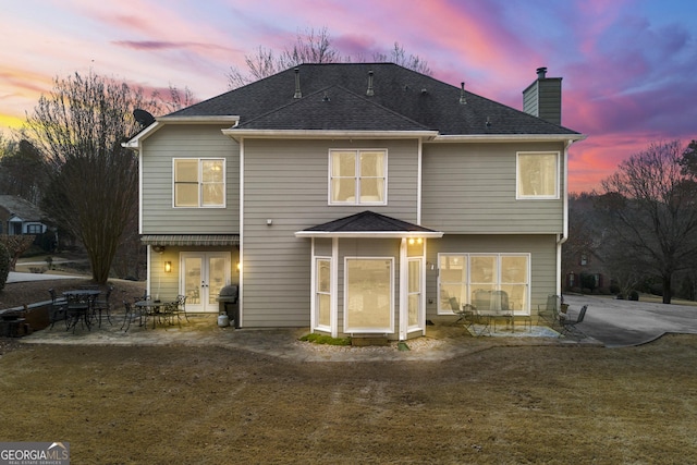 back of property at dusk featuring french doors, a chimney, a patio, and roof with shingles