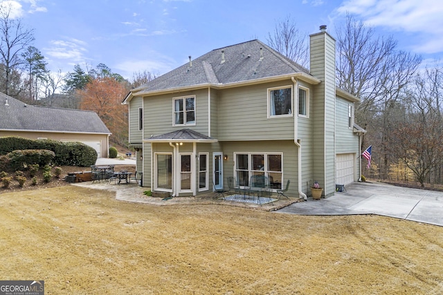 back of house featuring driveway, a shingled roof, a garage, a chimney, and a patio area