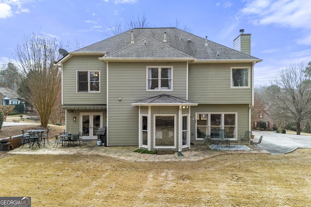 back of house featuring a patio, french doors, roof with shingles, and a chimney