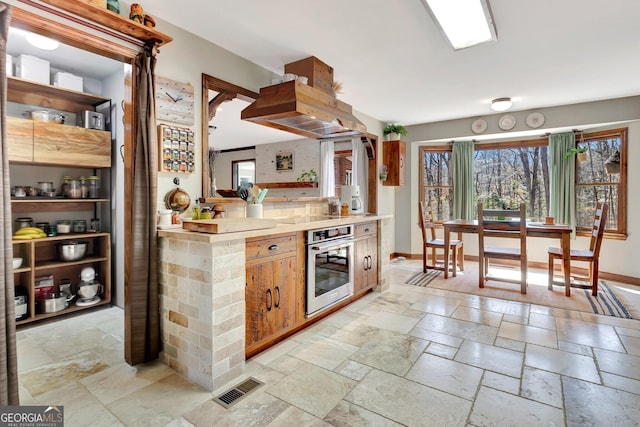 kitchen with stone tile floors, baseboards, visible vents, light countertops, and stainless steel oven