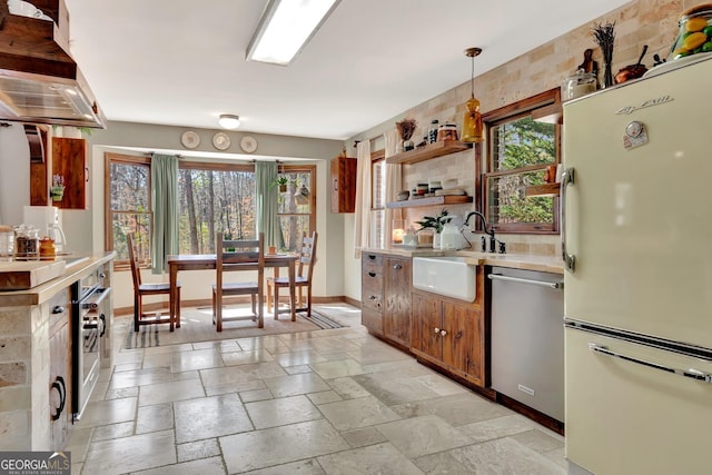 kitchen with stone tile floors, baseboards, freestanding refrigerator, light countertops, and stainless steel dishwasher