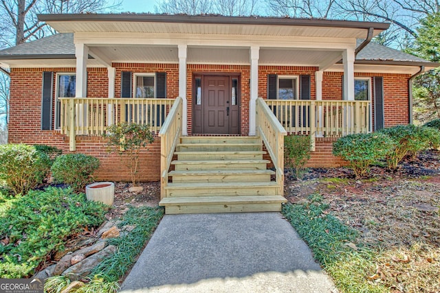 entrance to property featuring brick siding, a porch, and roof with shingles