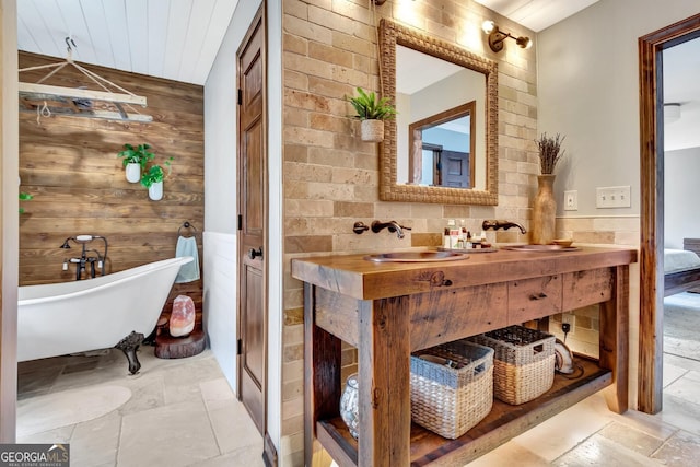 bathroom with vanity, wooden walls, a soaking tub, stone tile flooring, and wainscoting