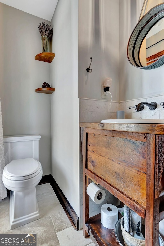 half bathroom with baseboards, toilet, and vanity